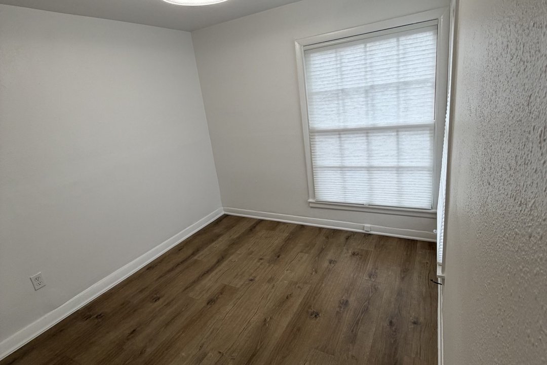 Bedroom in Unit C with new ceiling light and large window, hardwood-look flooring