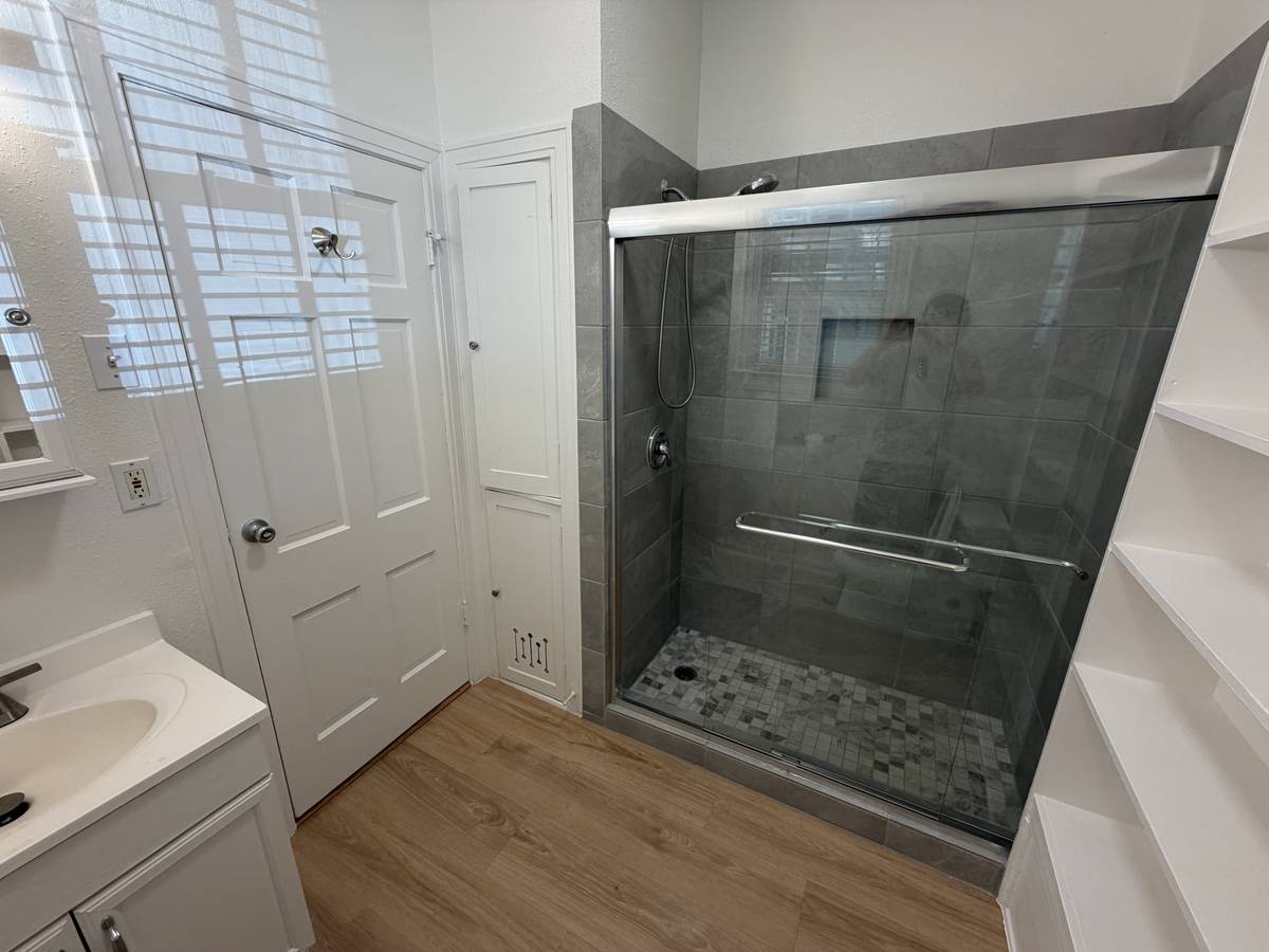 Completely renovated bathroom in Unit D with a grey-tiled walk-in shower, glass doors and new flooring