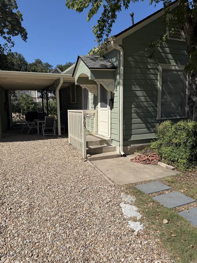 Exterior of Unit D — sage green cottage with a covered porch, carport and shaded seating area